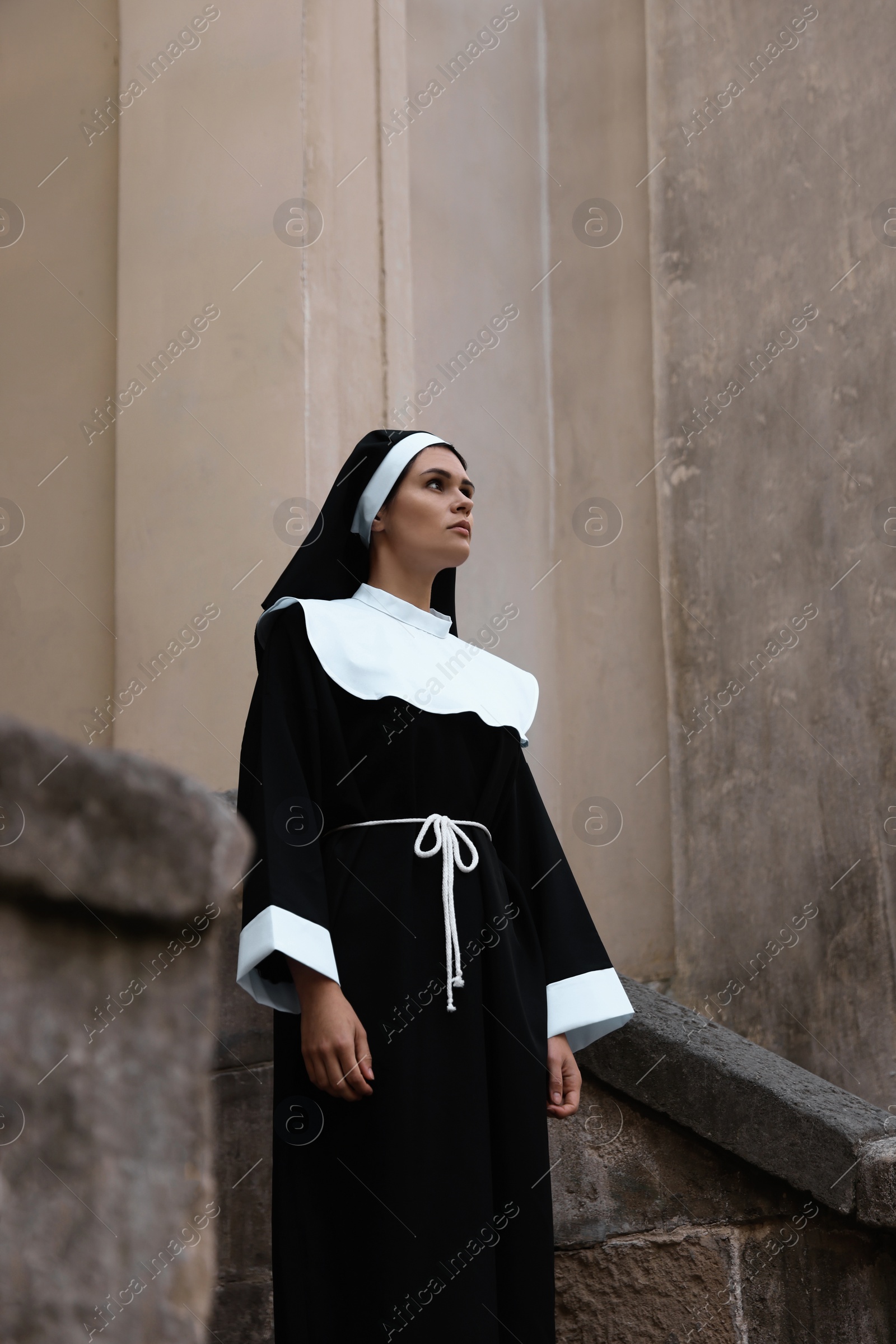 Photo of Beautiful young nun in cassock near building outdoors