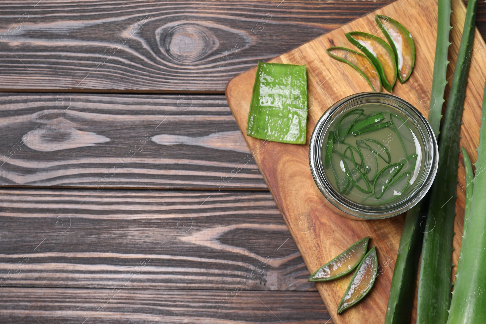 Photo of Fresh aloe juice in jar and leaves on wooden table, top view. Space for text