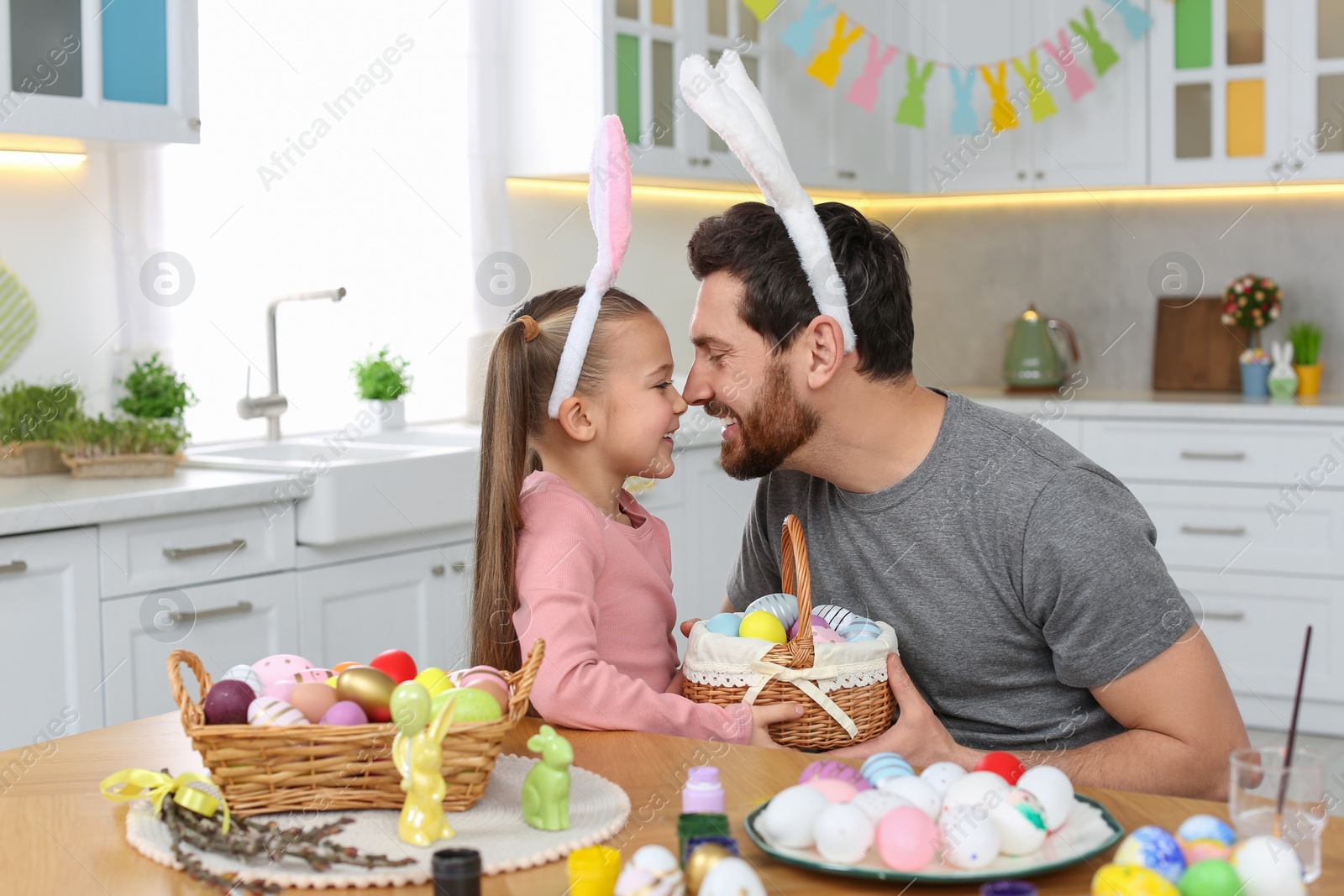 Photo of Father and his cute daughter with wicker basket full of Easter eggs in kitchen