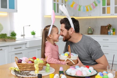 Father and his cute daughter with wicker basket full of Easter eggs in kitchen