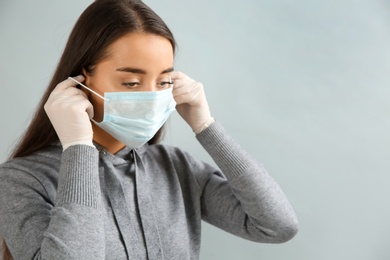 Photo of Woman in medical gloves putting on protective face mask against grey background