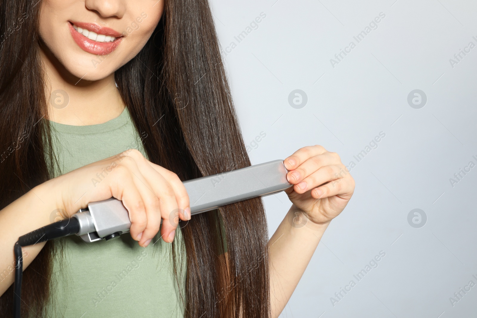 Photo of Happy woman using hair iron on grey background, closeup. Space for text