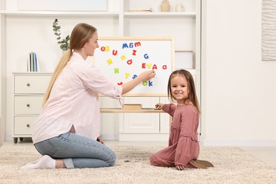 Mom teaching her daughter alphabet with magnetic letters at home