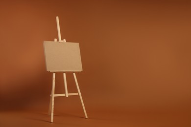 Wooden easel with blank board on brown background. Space for text