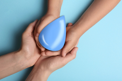 Woman and her child holding water drop on light blue background, top view. Ecology protection