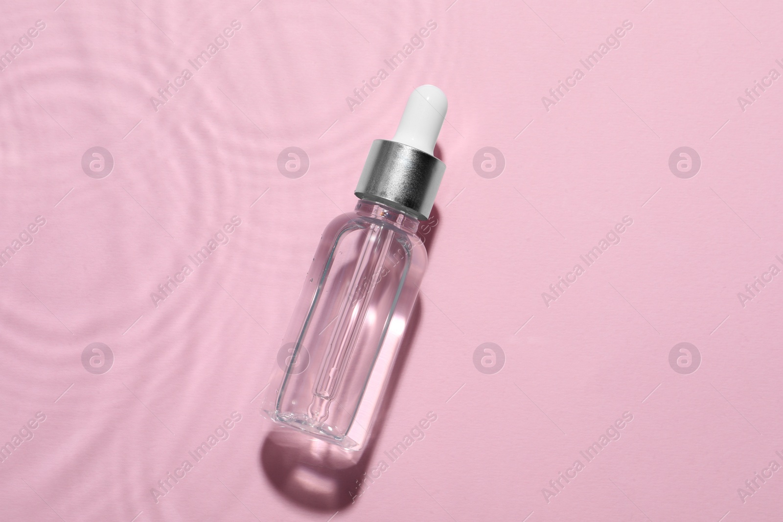 Photo of Bottle of cosmetic oil in water on pink background, top view