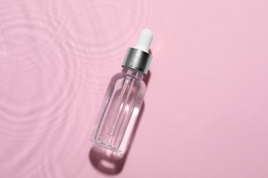 Photo of Bottle of cosmetic oil in water on pink background, top view