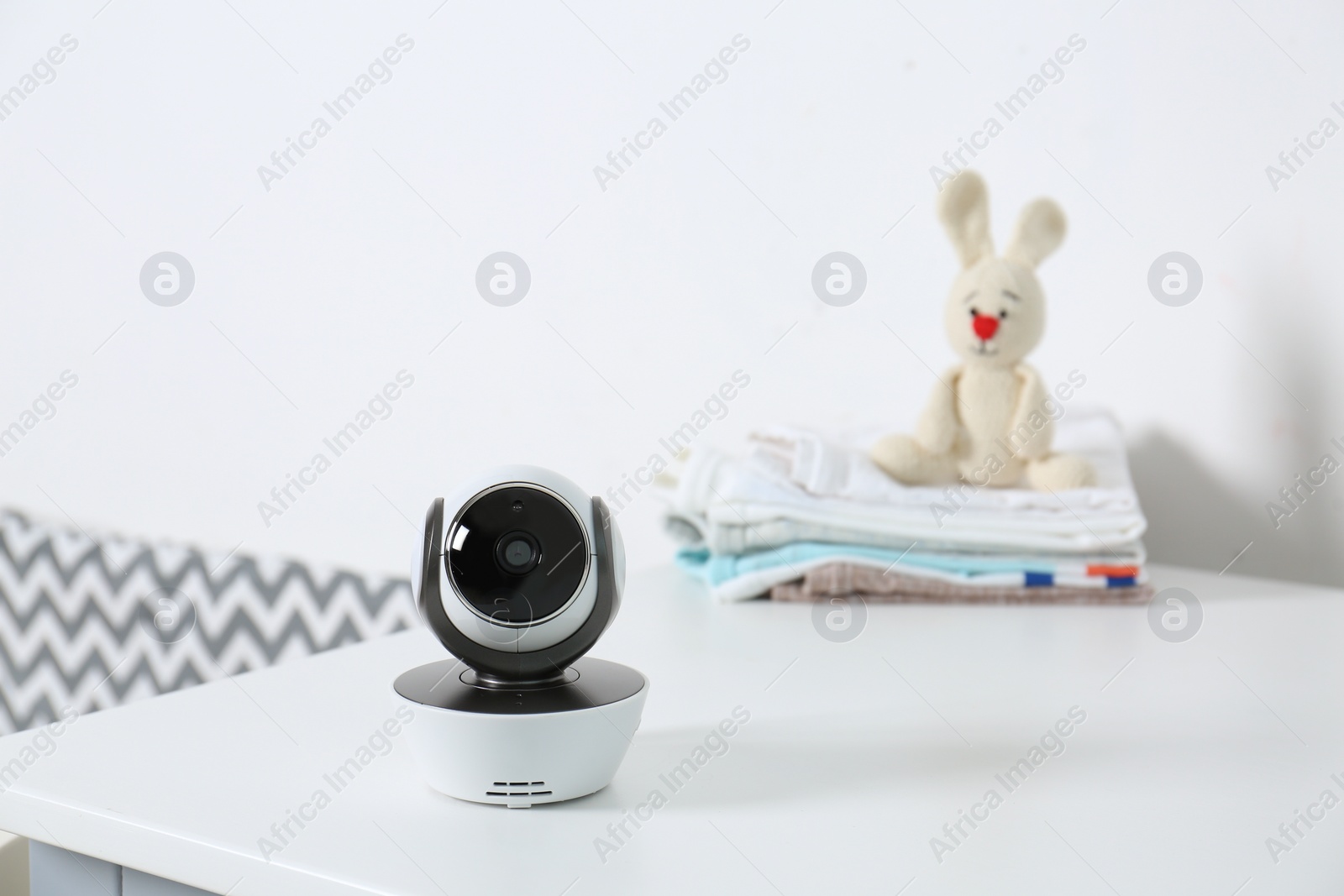 Photo of Baby camera with toy and clothes on table near white wall in room, space for text. Video nanny