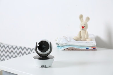 Photo of Baby camera with toy and clothes on table near white wall in room, space for text. Video nanny