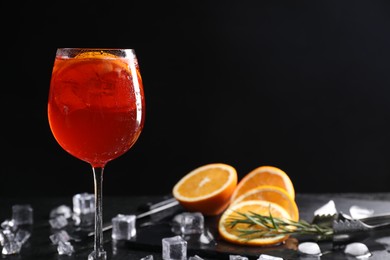 Glass of tasty Aperol spritz cocktail with orange slices and ice cubes on table against black background, space for text