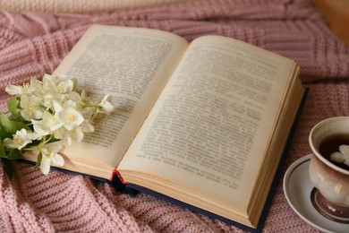 Photo of Open book, cup of aromatic tea and beautiful jasmine flowers on pink fabric