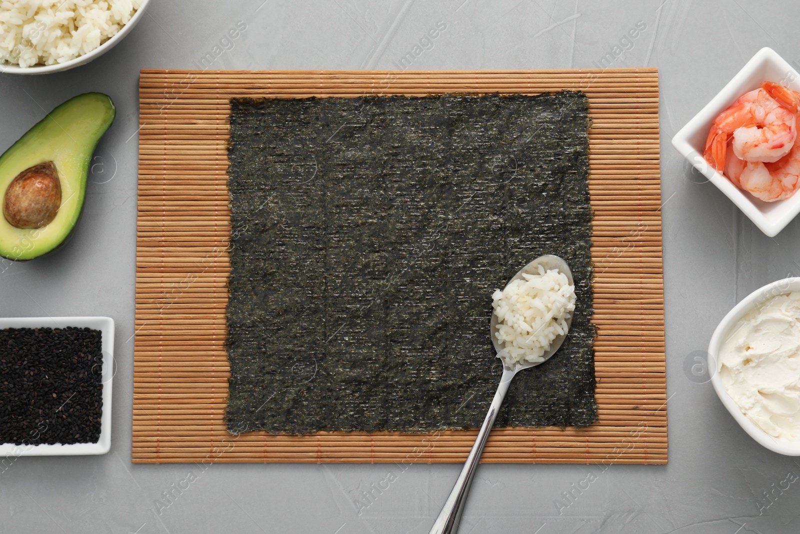 Photo of Cooking sushi. Nori, spoon with rice and other ingredients on grey textured table, flat lay