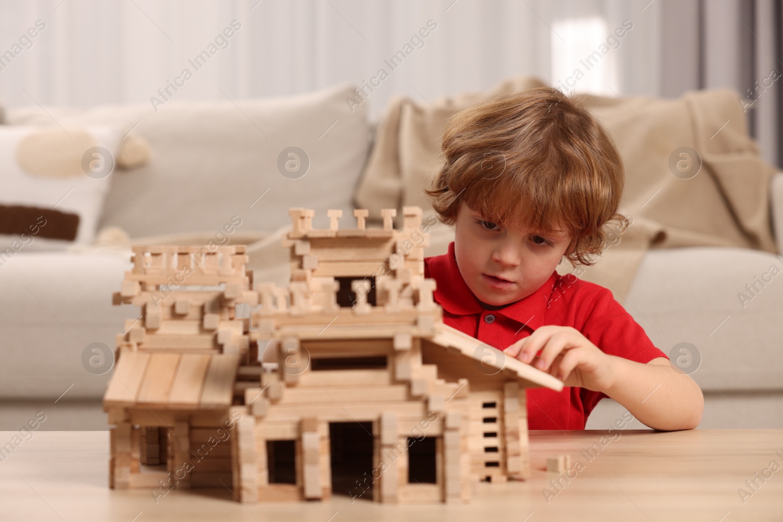 Photo of Cute little boy playing with wooden castle at table in room. Child's toy