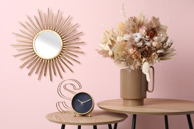 Stylish ceramic vase with dry flowers and leaves on wooden table near pink wall