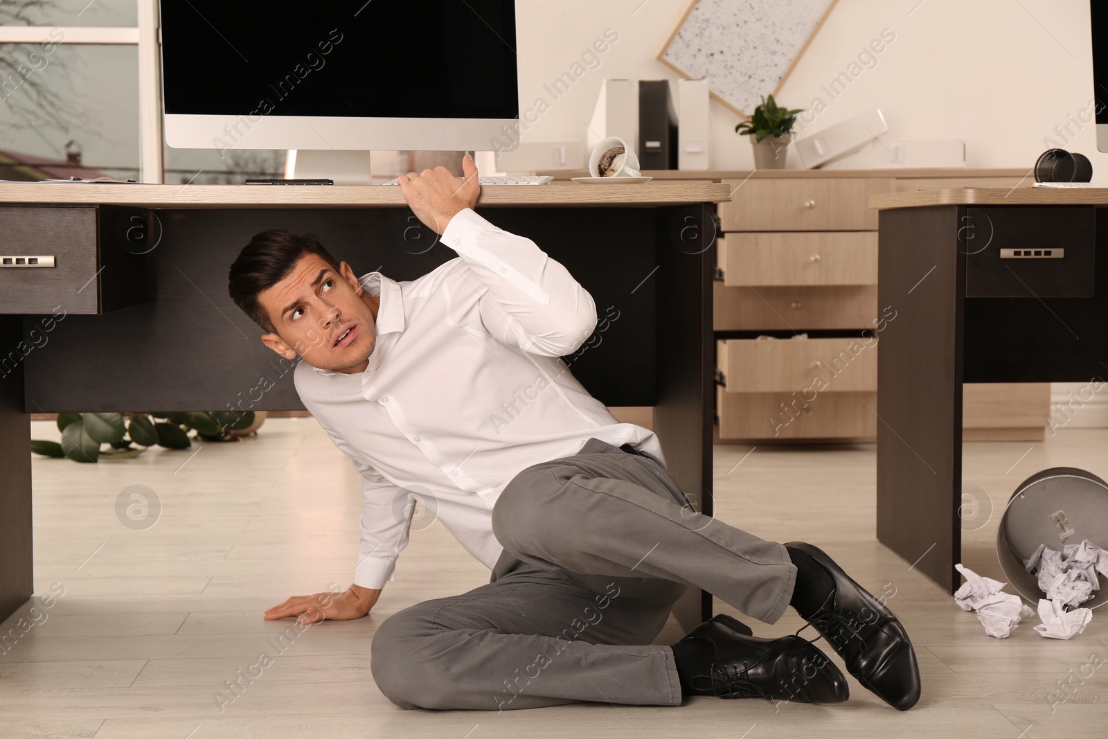 Photo of Scared man hiding under office desk during earthquake