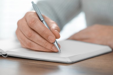 Man writing in notebook at wooden table, closeup