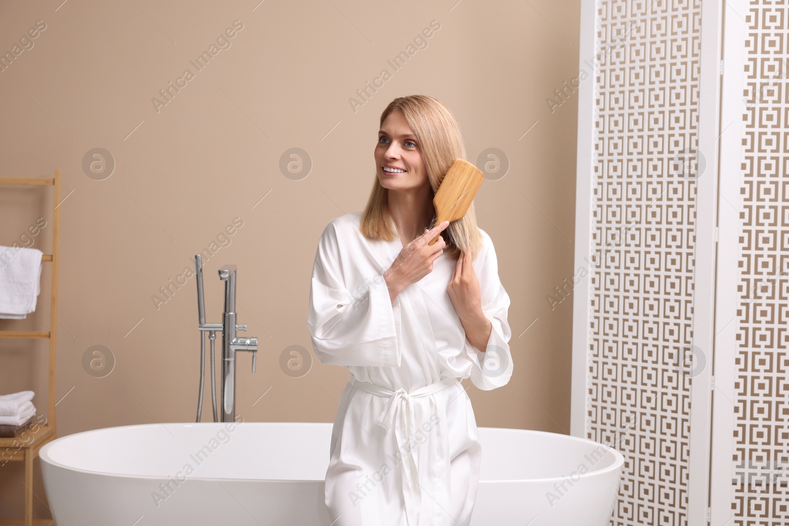 Photo of Beautiful woman brushing her hair near tub in bathroom