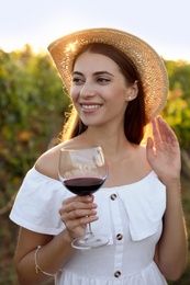 Beautiful young woman with glass of wine in vineyard on sunny day