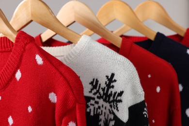 Different Christmas sweaters hanging on rack against light background, closeup