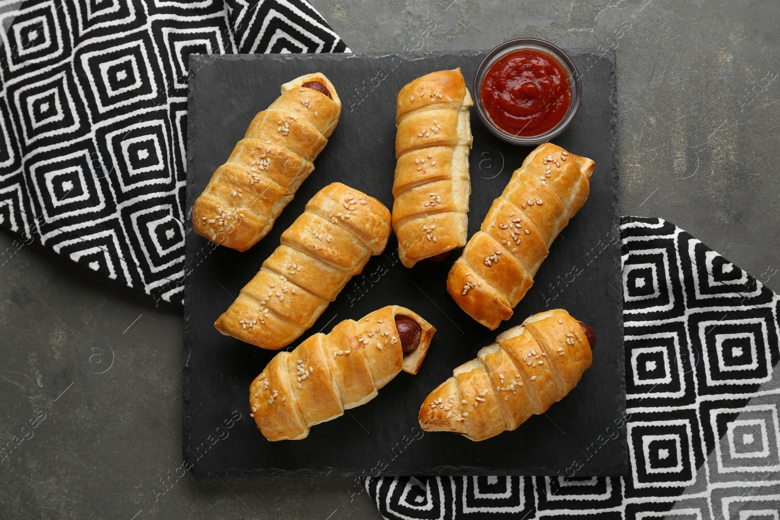 Photo of Delicious sausage rolls and ketchup on grey table, top view