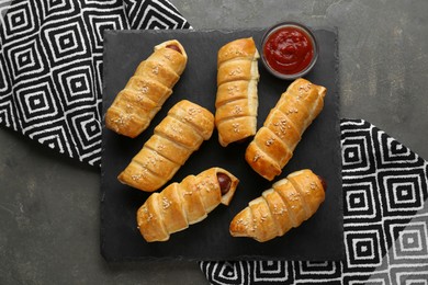 Photo of Delicious sausage rolls and ketchup on grey table, top view