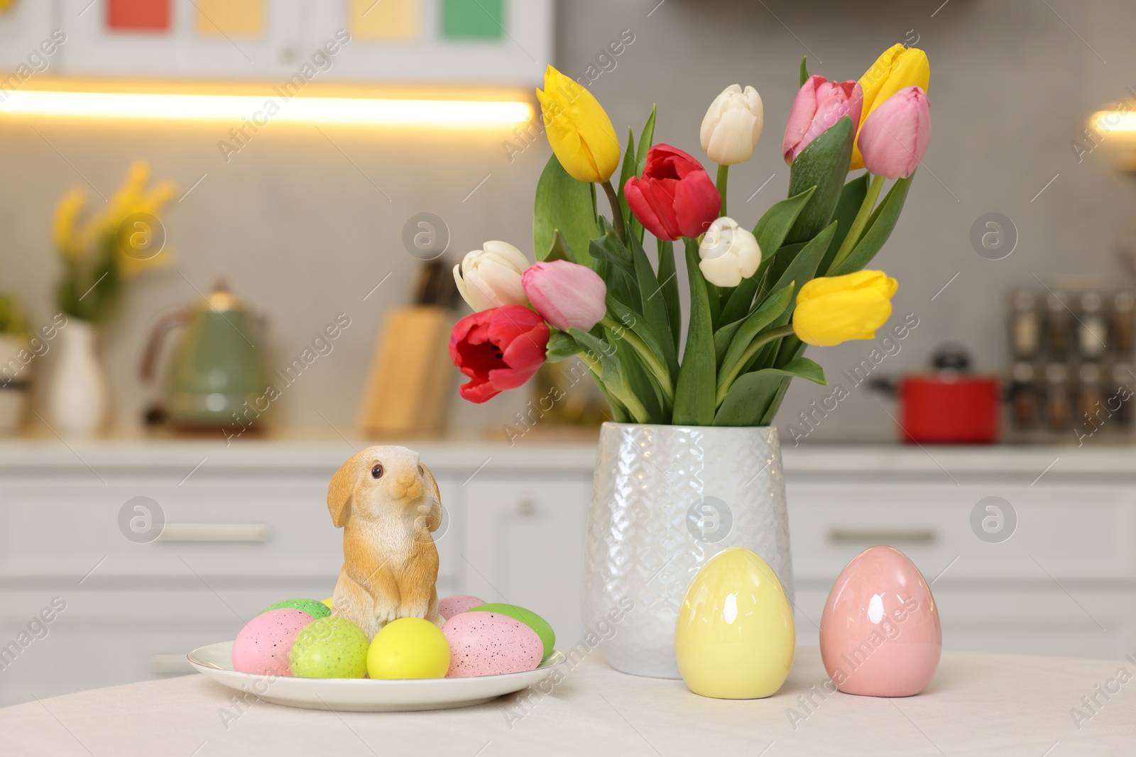 Photo of Bouquet of tulips, painted eggs and Easter decorations on white table in kitchen