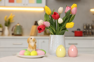 Bouquet of tulips, painted eggs and Easter decorations on white table in kitchen