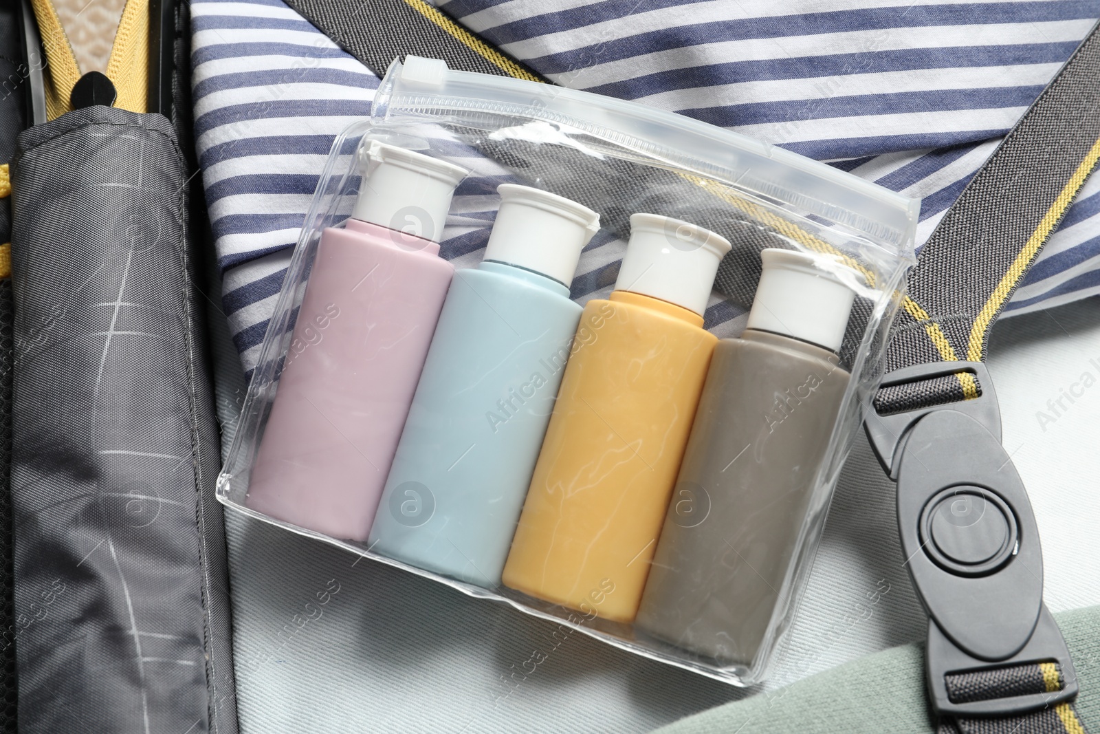 Photo of Plastic bag of cosmetic travel kit and clothes in suitcase, top view