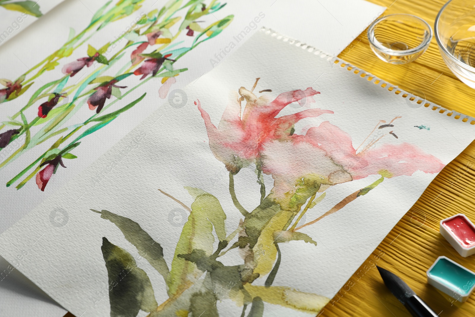 Photo of Beautiful floral pictures and watercolor paints on yellow wooden table