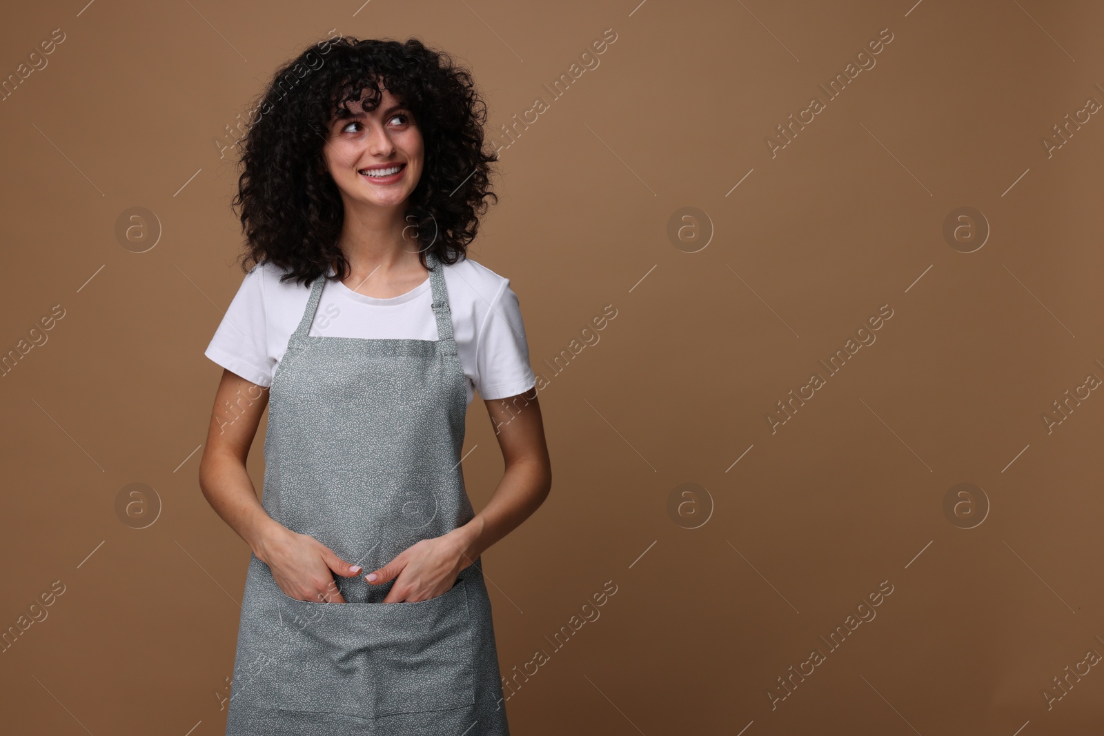 Photo of Happy woman wearing kitchen apron on brown background. Mockup for design