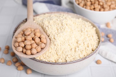 Chickpea flour in bowl and seeds on white tiled table, closeup
