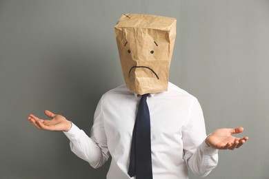 Photo of Man wearing paper bag with drawn sad face on grey background