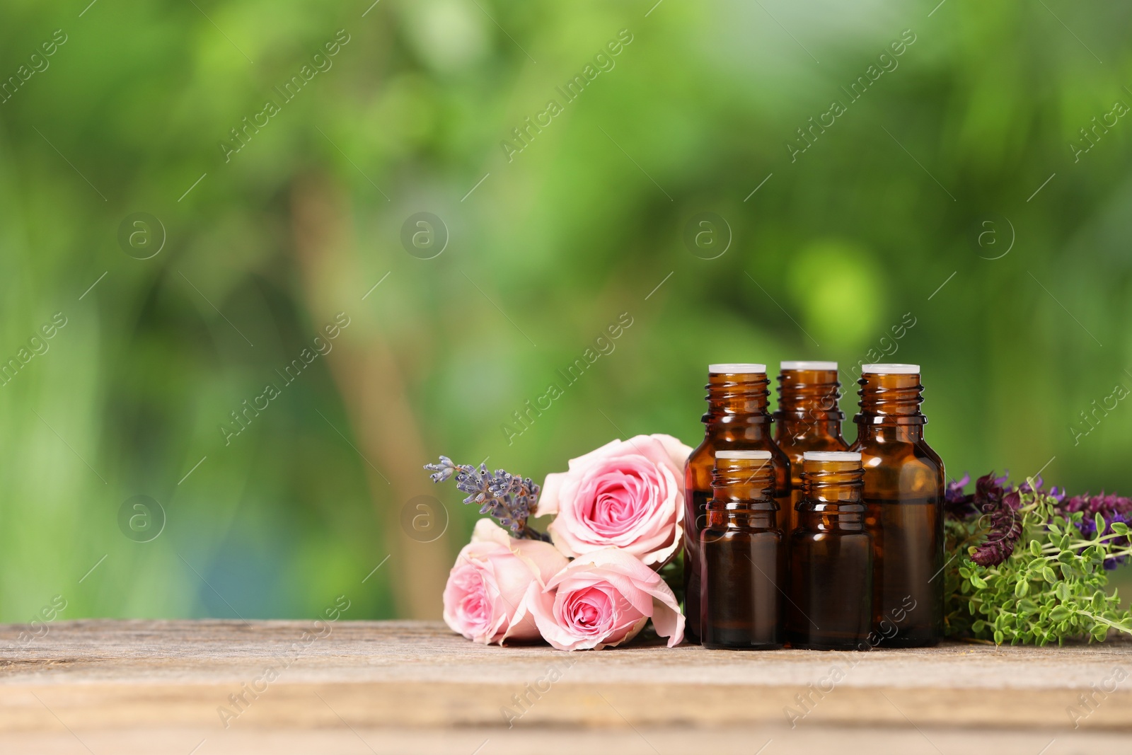 Photo of Bottles with essential oils, herbs and flowers on wooden table against blurred green background. Space for text