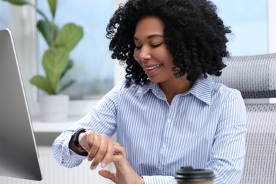 Photo of Young woman checking time on watch at workplace in office
