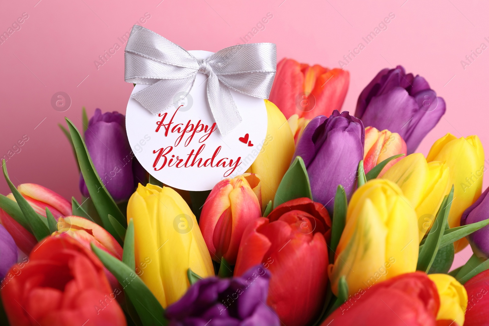 Image of Beautiful bouquet of tulip flowers with Happy Birthday card on pink background, closeup