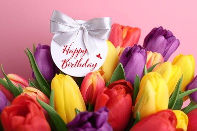 Beautiful bouquet of tulip flowers with Happy Birthday card on pink background, closeup