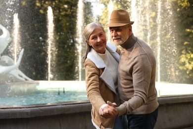 Affectionate senior couple dancing together near fountain outdoors, space for text