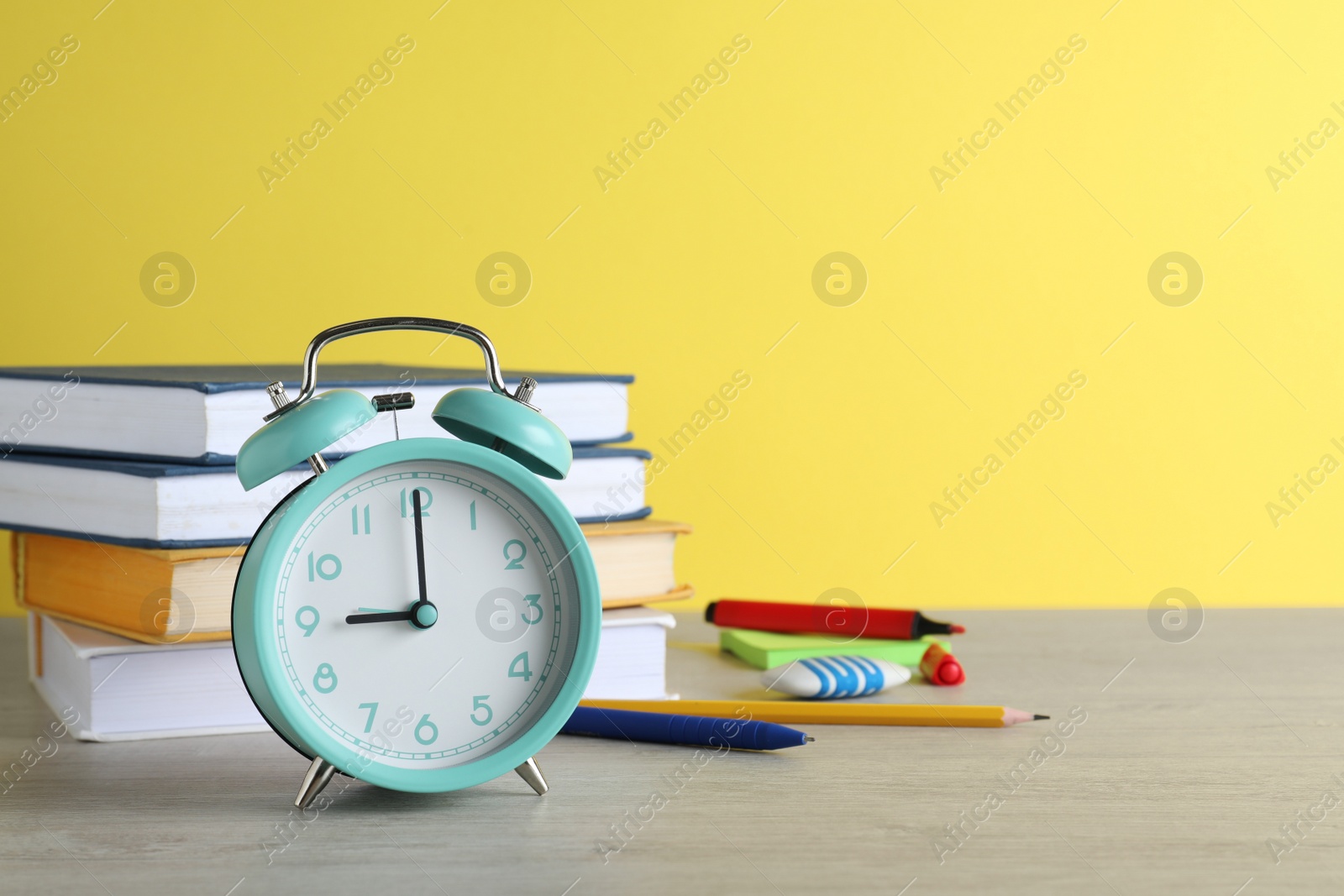 Photo of Turquoise alarm clock and different stationery on white wooden table against yellow background, space for text. School time