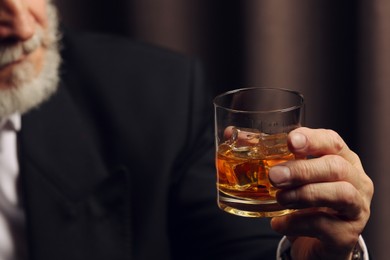 Photo of Man holding glass of whiskey with ice cubes on dark background, closeup