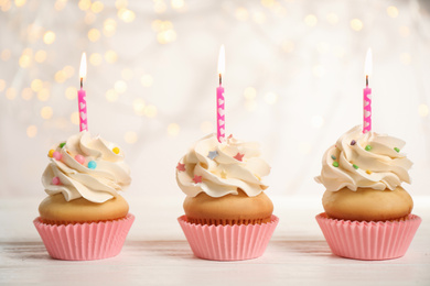 Birthday cupcakes with candles on white wooden table against blurred lights