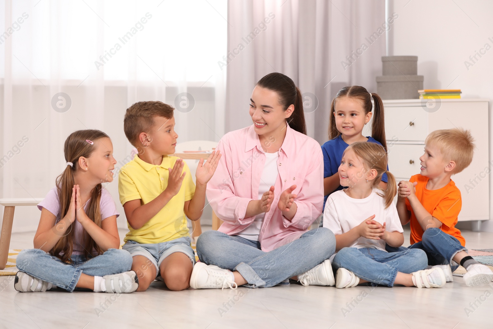 Photo of Nursery teacher and group of cute little children spending time together on floor in kindergarten. Playtime activities