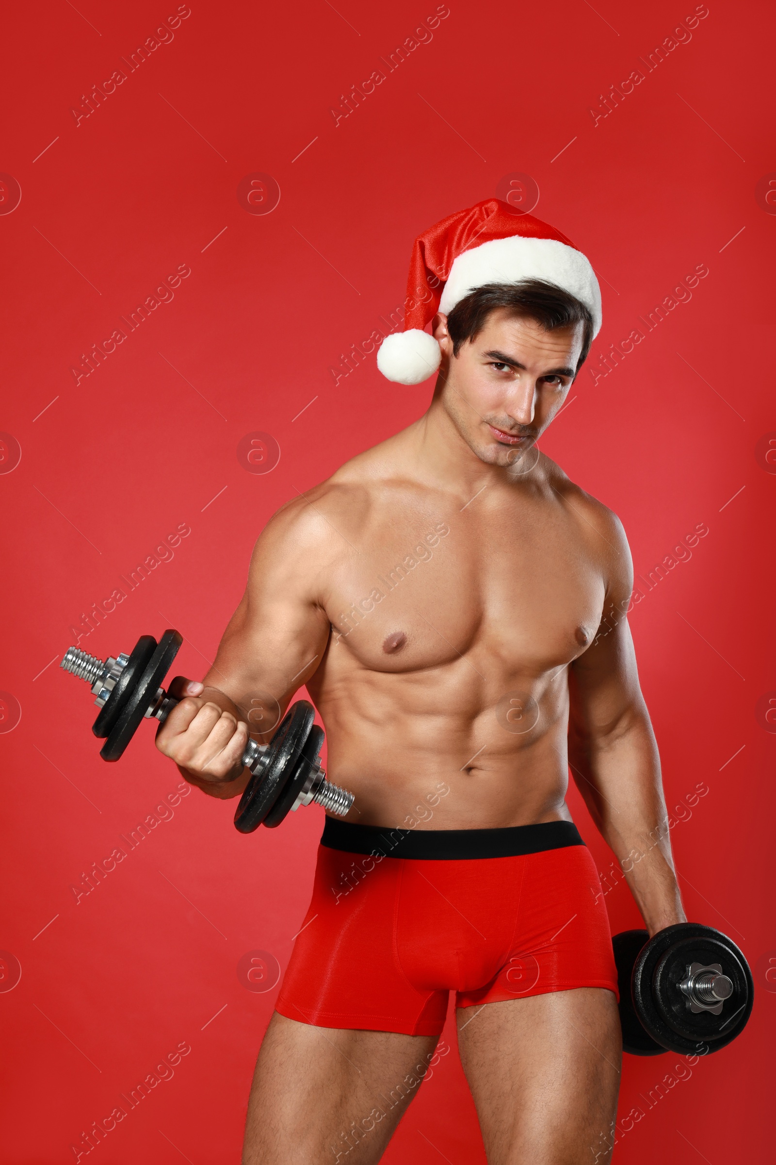 Photo of Sexy shirtless Santa Claus with dumbbells on red background