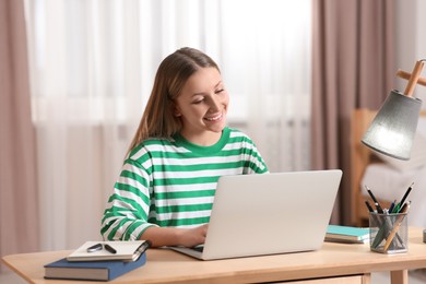 Photo of Online learning. Smiling teenage girl typing on laptop at home