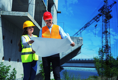 Image of Professional engineers in safety equipment with drafting  at construction site