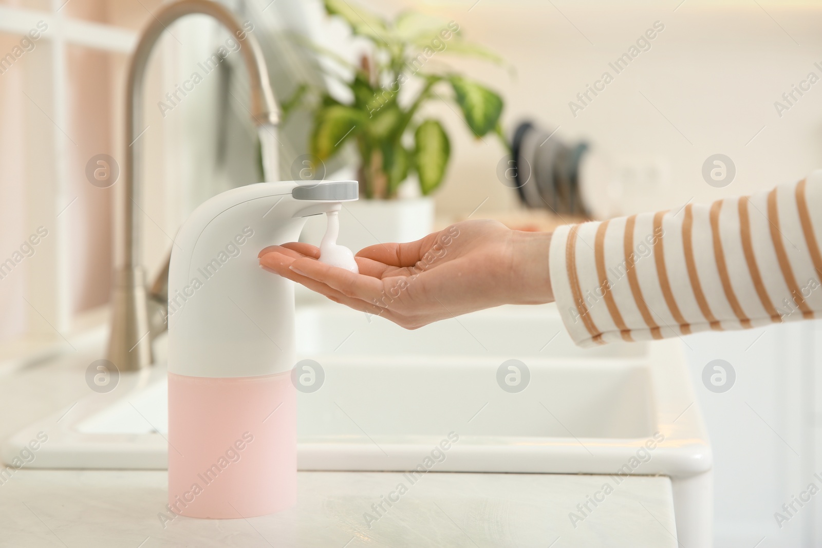 Photo of Woman using automatic soap dispenser in kitchen, closeup