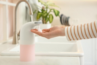 Woman using automatic soap dispenser in kitchen, closeup