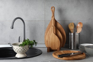 Photo of Wooden cutting boards, other cooking utensils and dishware on light grey countertop in kitchen