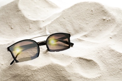 Stylish sunglasses on white sand. Space for text