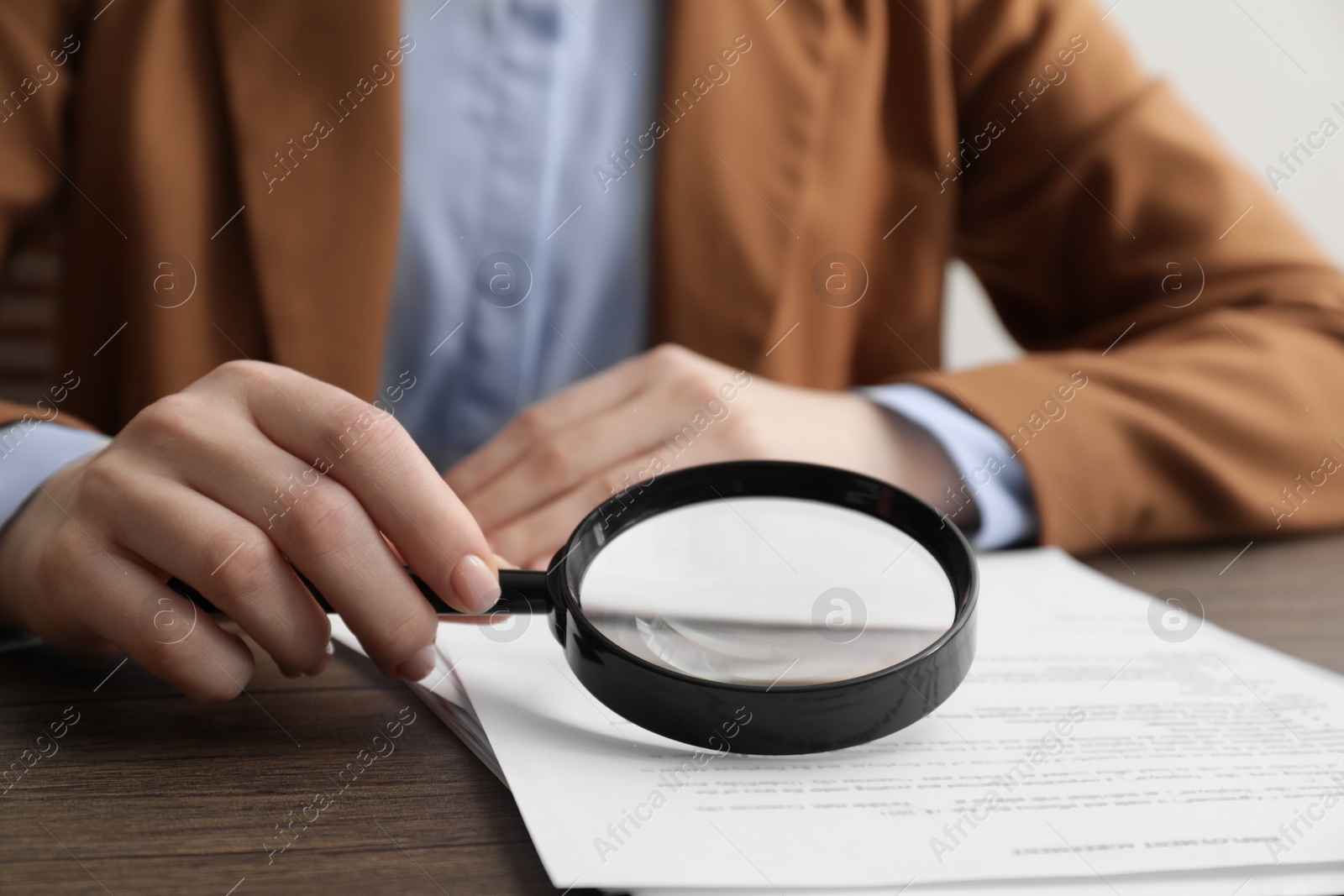 Photo of Woman looking at document through magnifier at wooden table, closeup. Searching concept