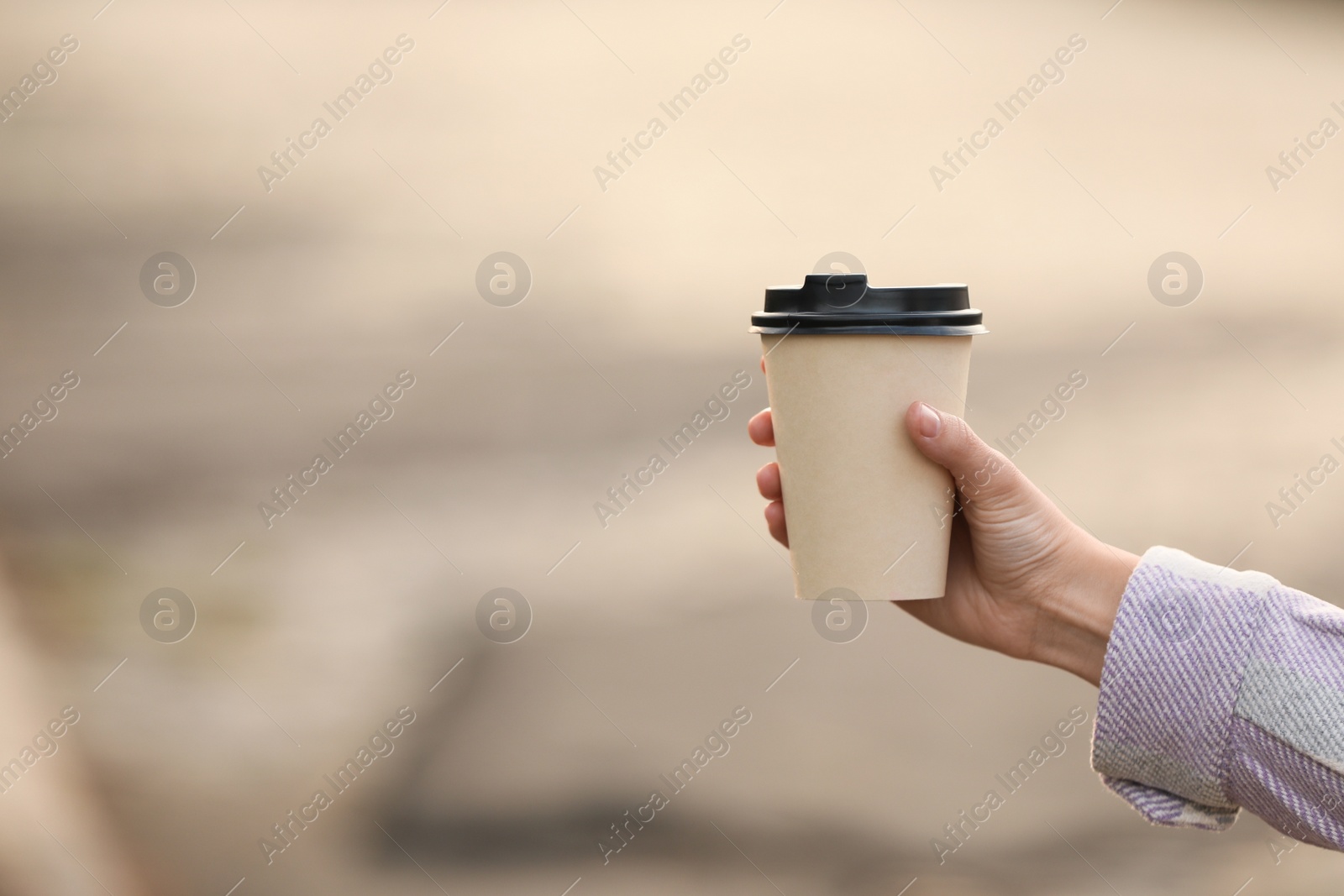 Photo of Woman holding paper coffee cup on blurred background, closeup. Space for text